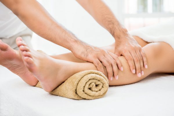 Hands of male therapist (masseur) giving massage to a woman leg