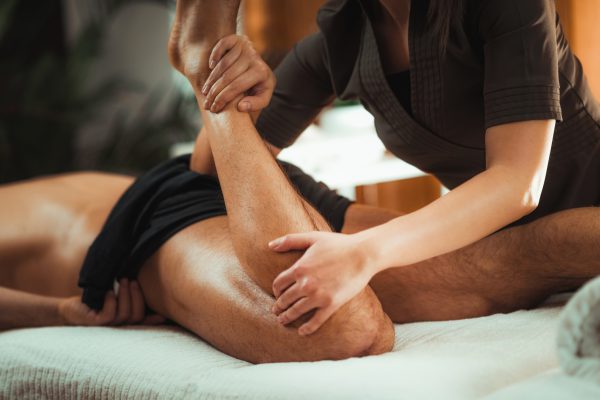 Physiotherapist massaging male patient with injured leg muscle. Sports injury treatment.